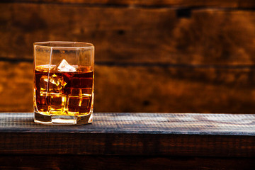 Whiskey with ice or brandy in a glass and a square carafe on an old wooden background. Whiskey with ice in a glass. Whiskey or cognac. Selective focus.