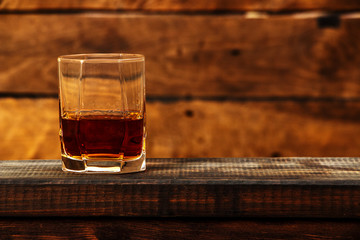 Whiskey with ice or brandy in a glass and a square carafe on an old wooden background. Whiskey with ice in a glass. Whiskey or cognac. Selective focus.