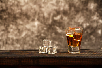 Whiskey with ice or brandy in a glass and a square carafe on an old wooden background. Whiskey with ice in a glass. Whiskey or cognac. Selective focus.