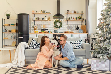 Married couple with husky dog sitting on the floor over couch and christmas tree