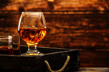 Whiskey with ice or brandy in a glass and a square carafe on an old wooden background. Whiskey with...