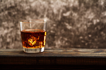 Whiskey with ice or brandy in a glass and a square carafe on an old wooden background. Whiskey with ice in a glass. Whiskey or cognac. Selective focus.