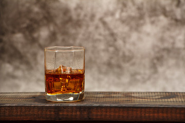 Whiskey with ice or brandy in a glass on a background of gray concrete on an old wooden table. Whiskey with ice in a glass. Whiskey or brandy. Selective focus.