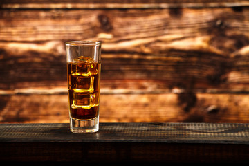 Whiskey with ice or brandy in a glass and a square carafe on an old wooden background. Whiskey with ice in a glass. Whiskey or cognac. Selective focus.