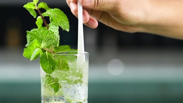 Pouring soda in Refreshing peppermint cocktail. Non-alcoholic drink with lemon mint and ice call Mocktail . Carbonated water and soda make small bubbles fizzy drink in a glass in pool background.