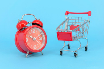 Shopping cart and classic alarm clock on blue background. Sale time buy mall market shop consumer...