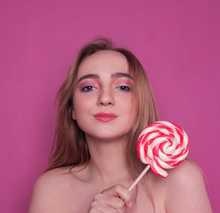 portrait of a beautiful fashionable blonde girl smiling, holding a multi-colored Lollipop on a pink background