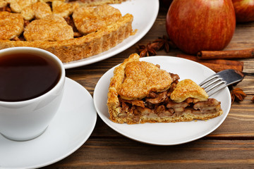Closeup piece of homemade apple pie with cinnamon and cup of tea on wooden table. Shallow focus.
