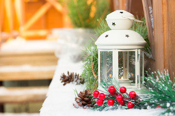 White Christmas lantern in snow, with yellow candle light, on wooden background