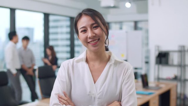 Portrait of successful beautiful executive businesswoman smart casual wear looking at camera and smile, arms crossed in modern office workplace. Young Asia lady standing in contemporary meeting room.