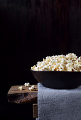 Popcorn in a black ceramic bowl on a wooden table against dark background
