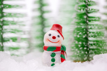 Happy snowman on snow with background of blurred Christmas pine. Miniature people in Christmas Theme.  