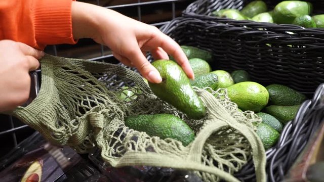 Young woman picking veggies and fruits in supernarket in mesh organic shopping bag, zero waste