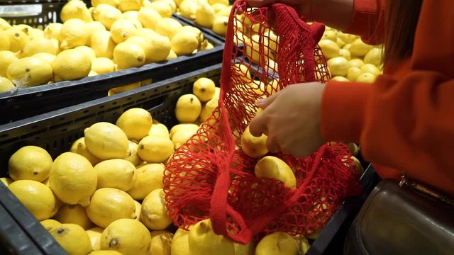 Young woman picking veggies and fruits in supernarket in mesh organic shopping bag, zero waste