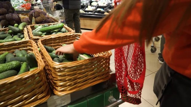 Young woman picking veggies and fruits in supernarket in mesh organic shopping bag, zero waste