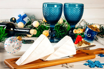 Brie cheese, a bottle of wine, coniferous green branches on a wooden background. Goodies for the holiday. The concept of Christmas and the New year. Toned