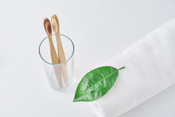 Two wooden bamboo eco friendly toothbrushes in glass and towel on a white background.  Dental care...