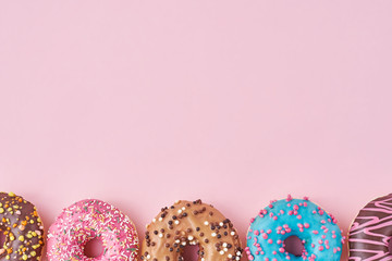 Different types of a colorful donats decorated sprinkles and icing on pastel pink background with copy space