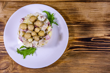 Salad with marinated mushrooms, sausage, onion, boiled potato and mayonnaise on a wooden table. Top view