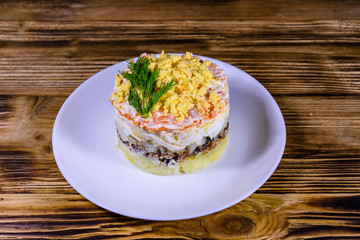Plate with traditional russian salad Mimosa on a wooden table. Layered salad with potatoes, sardine, cheese, carrot, eggs and mayonnaise