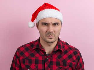 Emotions on the face, indifference and disgust. A man in a plaid rabbit and a Christmas red hat, on a pink background, copy space.
