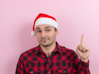 Emotions on the face, pensive, reflection, plan, idea. A man in a plaid rabbit and a Christmas red hat, on a pink background, copy space.