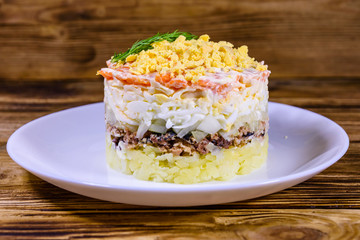 Plate with traditional russian salad Mimosa on a wooden table. Layered salad with potatoes,...