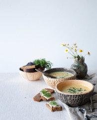 Cheese soup with mushrooms and vegetables, brown bread with butter, dill and basil on a white wooden background