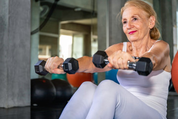Fototapeta na wymiar Senior woman Caucasian training arm with dumbell at fitness gym.