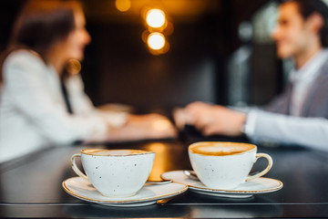 Close up image of two coffee cups with latte on wooden table in cafe.