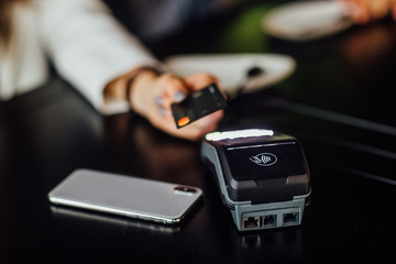 Picture showing people paying in restaurant by credit card reader. Phone on black table.