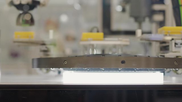 Conveyor with moving by probe arm details on automated control system with flashing scanner, people walking on background. Scanning computer-aided quality system. Automatic test set items scan on belt