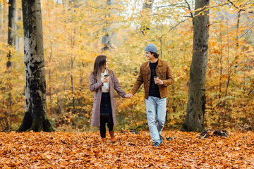 Fototapeta premium Family and hot autumn drink concept. Couple in love holding cups of tea or coffee and walking. Love story.