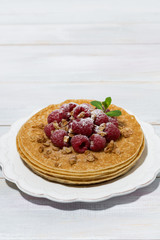 traditional thin pancakes with fresh raspberries on plate on wooden table, vertical