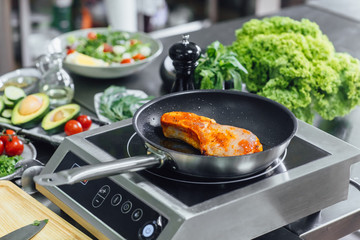 Close up photo, preparing delicious fishes on frying pan, professional white kitchen with equipment.