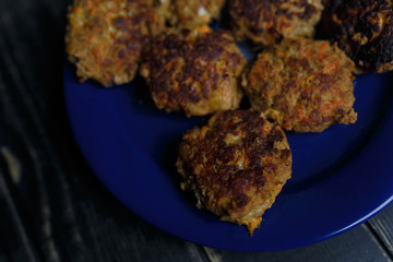 Meat and carrot cutlets on blue plate standing on black wooden background. Tasty unhealthy food. Diet, nutrition, eating habits concept. Place for text
