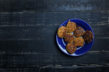 Meat and carrot cutlets on blue plate standing on black wooden background. Tasty unhealthy food. Diet, nutrition, eating habits concept. Place for text
