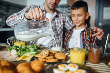 Father making breakfast for his kid at home. Cropped picture man hands pouring milk for flakes.