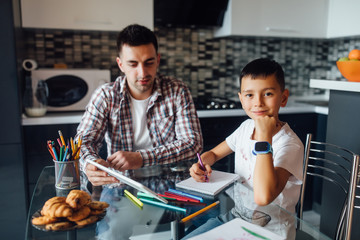 Handsome young father and his son using digital tablet for education and assisting him to learn lesson.