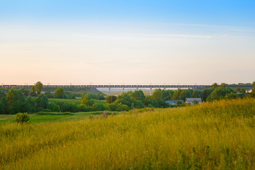 Fototapeta na wymiar Freight train passes on a railway bridge on the horizon near the village on a summer evening