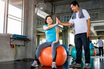 Asian senior couple smiling in sportswear exercising at gym.