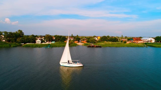 White sailing boat floating on the river near a small village. Copter ( drone ) shooting