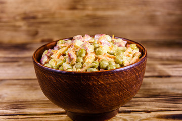 Salad with sausage, green pea, onion and carrot in glass bowl on wooden table