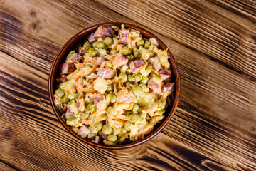 Salad with sausage, green pea, onion and carrot in glass bowl on wooden table. Top view