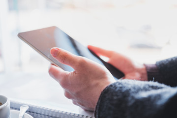 Human hands hold a tablet or e-book at a public place, close-up view. Web browsing, using technology on the go at the shopping mall, airport or food courts, shallow depth of field image in high key