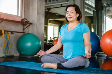 Senior fat woman Asian doing yoga exercise at fitness gym.