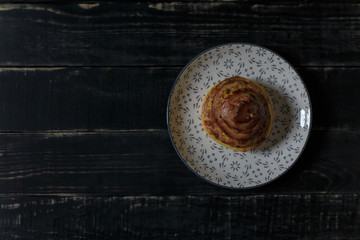 Cheese and dill bread bun on plate standing on black wooden background. Tasty unhealthy food. Diet, nutrition, eating habits concept. Place for text. 