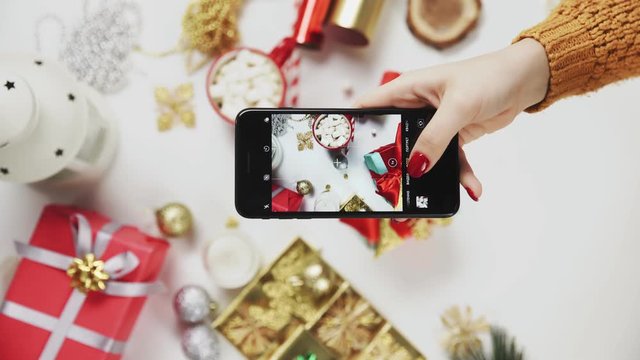 Woman taking beautiful picture on the smart phone. Female hands photogtaphing Christmas present on white table. Vertical Screen Orientation Video 9:16