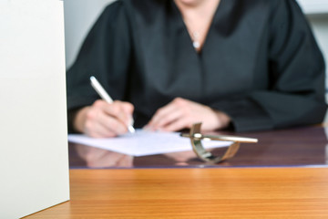 Concept: Female lawyer, out of focus in the background, in black robe works in her office with a book in the foreground – extreme blurred area for copy space and creative freedom