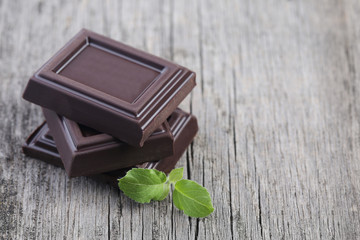 Dark chocolate with leaves on wooden background